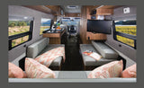 Inside a modern RV rental, featuring comfortable benches, a kitchen, TV, and large windows with beautiful outdoor views.