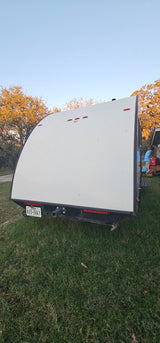 Rear view of a white Texas travel trailer (RV rental) parked on green grass, with a person loading items in the background.