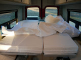 Inside a comfortable RV rental: a modular bed with white bedding, pillows, and scenic window views. Ideal for road trips.