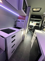 Modern RV rental: Sleek kitchen with induction cooktop, sink, white cabinets, and smart storage for comfortable travel.