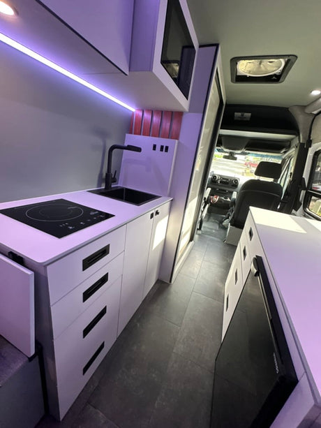 Modern RV rental: Sleek kitchen with induction cooktop, sink, white cabinets, and smart storage for comfortable travel.