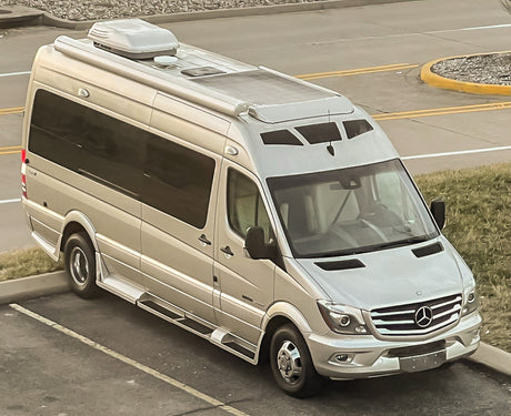 A silver Mercedes-Benz Sprinter RV rental parked outdoors, ready for travel adventures. Features solar panels and a rooftop AC unit.
