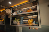 Clever RV rental storage: open shelves with bungee cords secure snacks, dishes, and decor for travel.