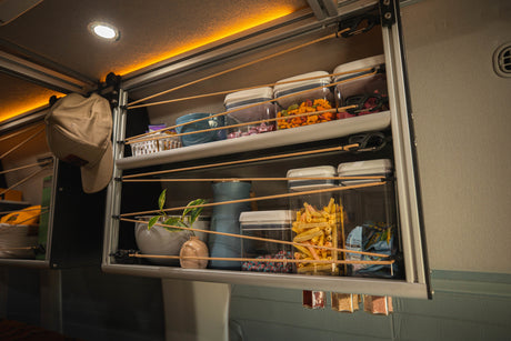 Clever RV rental storage: open shelves with bungee cords secure snacks, dishes, and decor for travel.