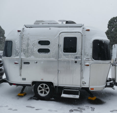 Snow-covered silver Airstream travel trailer, ideal for a cozy winter rv rental getaway.