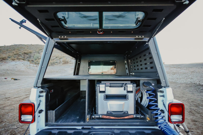View inside a truck bed camper with a slide-out fridge, organized storage, and utility hoses. Ideal for overland adventure or an RV rental alternative. — photo 7