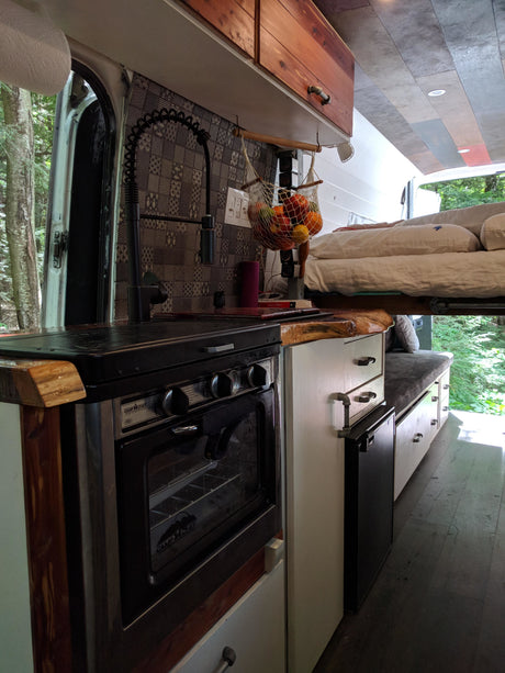 Cozy RV rental interior: Camper van with kitchen, bed, storage, and forest views through open doors.