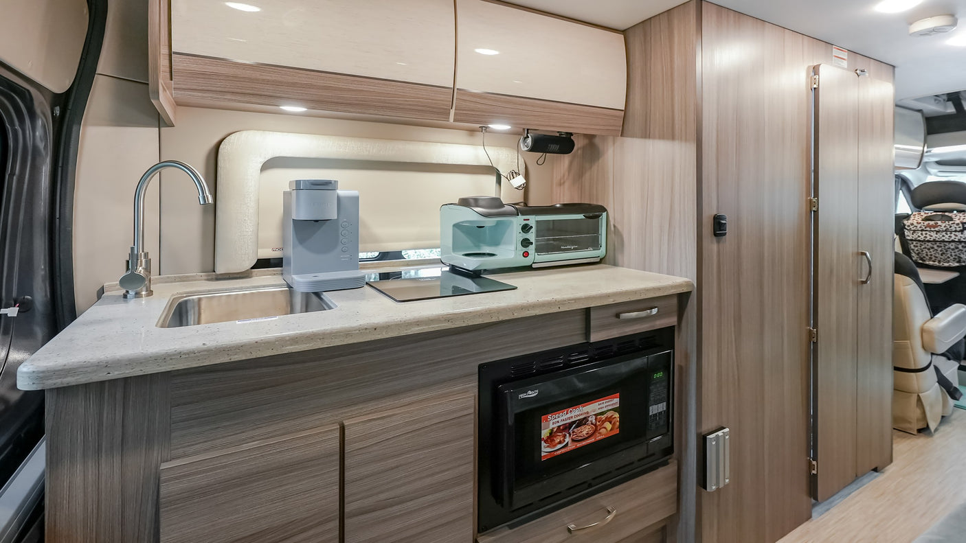 An RV rental kitchenette, showcasing its compact design with a sink, microwave, coffee maker, and toaster oven.