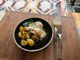 Breakfast with fried eggs, roasted potatoes, and spinach on a wooden surface in an RV rental. A refreshing drink and cutlery are ready.