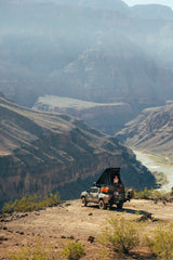 Person on a truck with rooftop tent overlooking a grand canyon and river. Perfect for adventure travel or an RV rental escape.