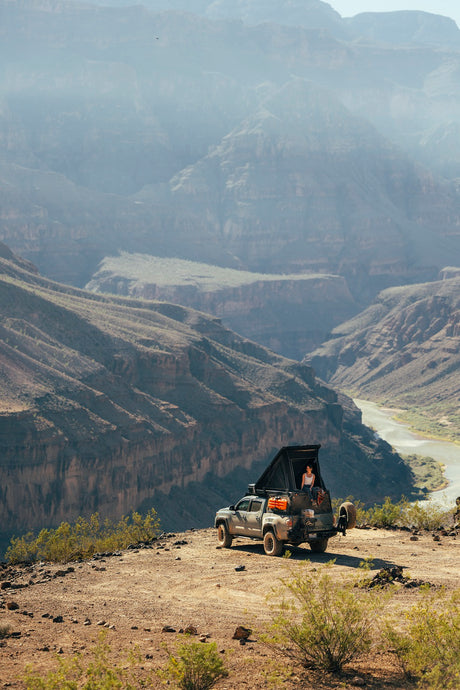 Person on a truck with rooftop tent overlooking a grand canyon and river. Perfect for adventure travel or an RV rental escape.