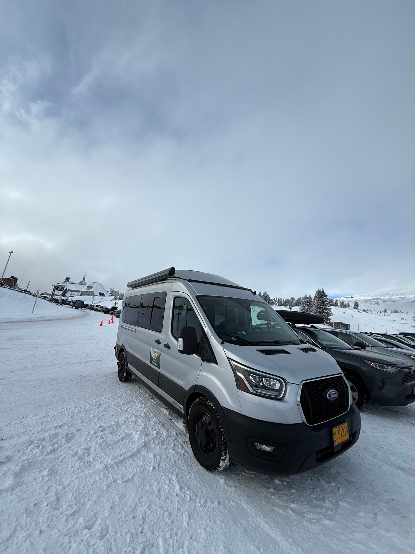 Silver Ford Transit RV rental van, from Outdoorsy, parked in a snowy mountain setting under cloudy skies. — photo 14