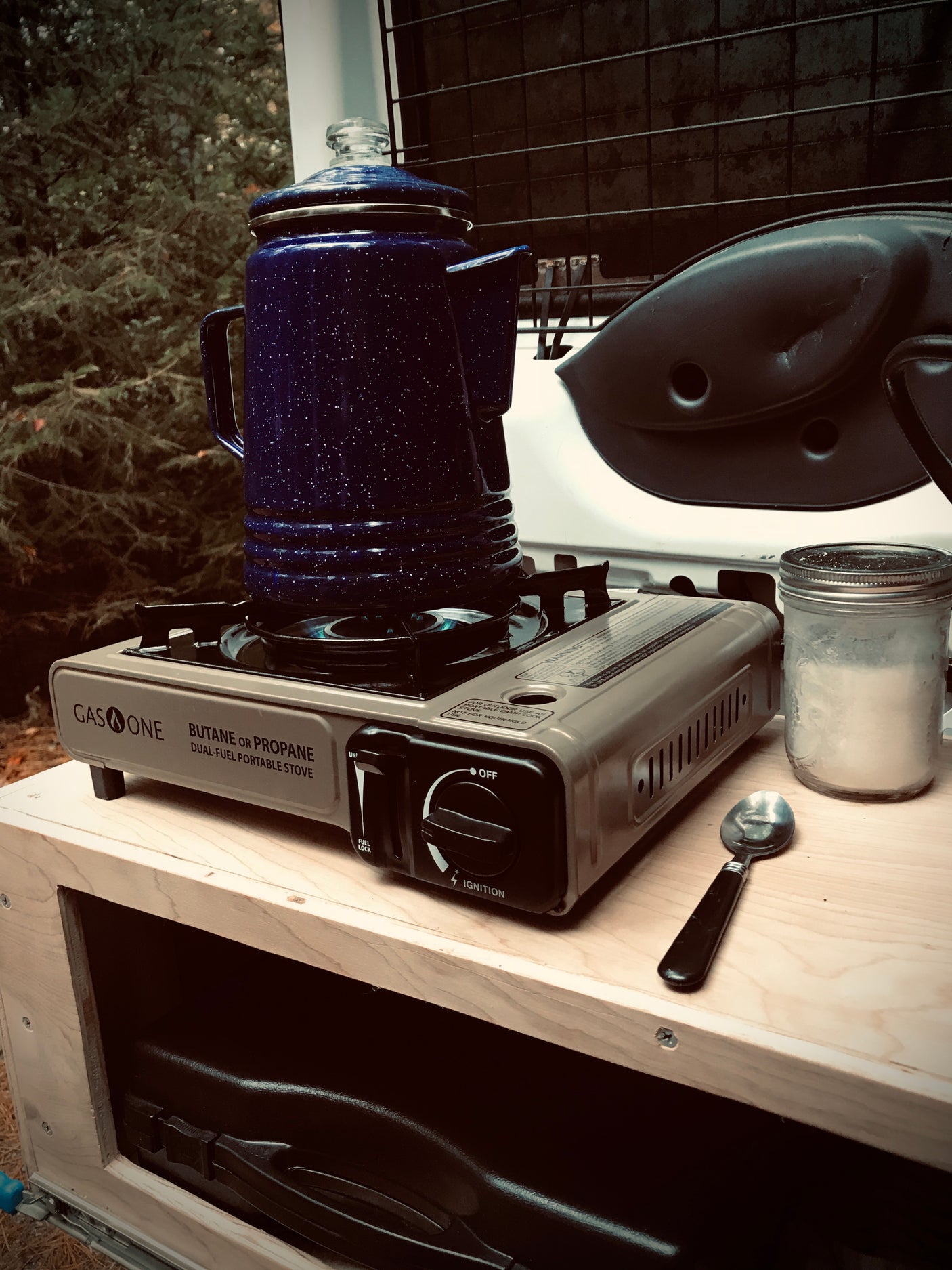 RV rental cooking setup: a blue percolator sits on a portable dual-fuel stove, ideal for brewing coffee while camping.