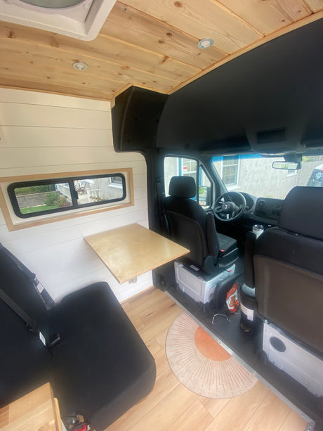 RV rental interior with warm wood ceiling, white shiplap walls, compact dining table, and cozy, functional design.
