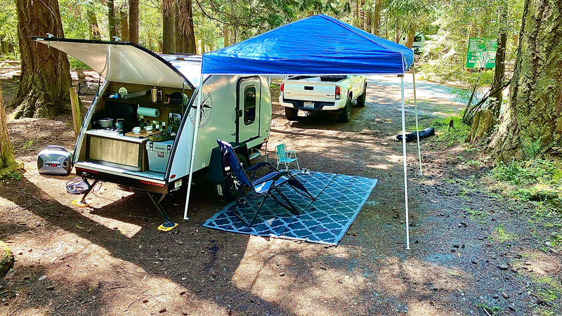 Relaxing rv rental setup: a teardrop camper with an open rear kitchen, canopy, and chairs in a serene forest campground. — photo 17