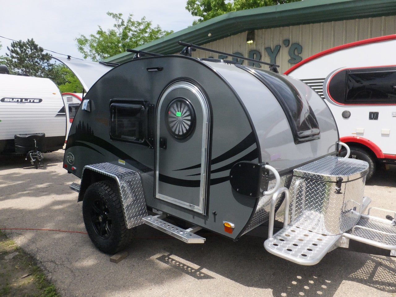 Compact dark grey teardrop RV rental and other campers on display at a dealership.