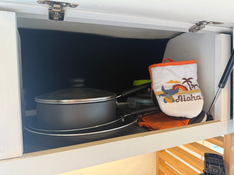 Efficient rv rental kitchen storage: stacked pots, pans, containers & a fun Stitch 'Aloha' oven mitt in an overhead cabinet.