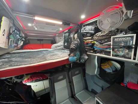 Functional RV rental interior with bunk bed, seating, and organized storage including gear for paragliding.