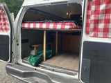 Back view of a DIY camper van conversion with a raised bed, storage, and checkered curtains, ideal for RV rental travel.