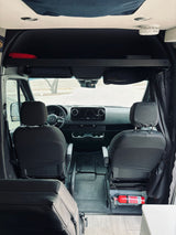 View of an RV rental's front cab from the rear, showing seats, dashboard, overhead shelf, and fire extinguisher.