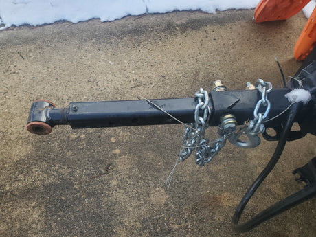 RV rental trailer hitch with safety chains on concrete pavement, featuring attachment bolts and a safety cable. Snow is present.