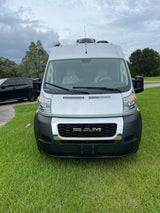 Silver Ram ProMaster van, ideal for an RV rental, parked on green grass. A black SUV is visible behind it.