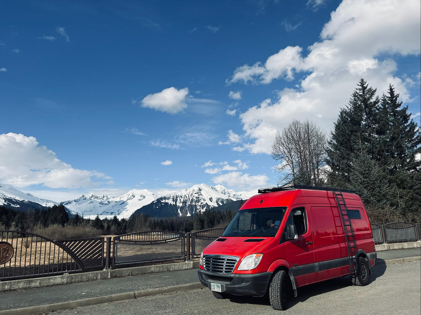 Bright red camper van (RV rental) against majestic snowy mountains under a bright blue sky. Explore nature!