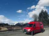 Bright red camper van (RV rental) against majestic snowy mountains under a bright blue sky. Explore nature!
