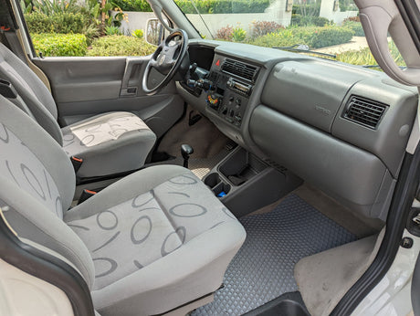 RV rental interior: spacious front cabin with gray seats, dashboard, and manual shifter.