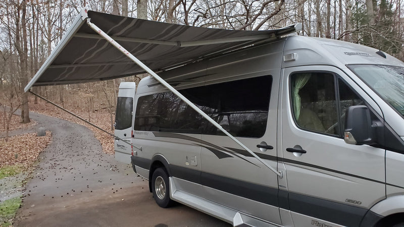  parked on a driveway among trees. Perfect for adventure!|Silver Pleasure-Way Sprinter **rv rental** with extended awning & open door — photo 6