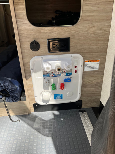 Detailed view of an RV rental's water management utility panel, showing various hookups, valves, and electrical outlets.