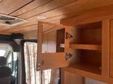 RV rental interior with beautiful wood paneling & functional cabinets. Open cabinet reveals storage & handy mirror.