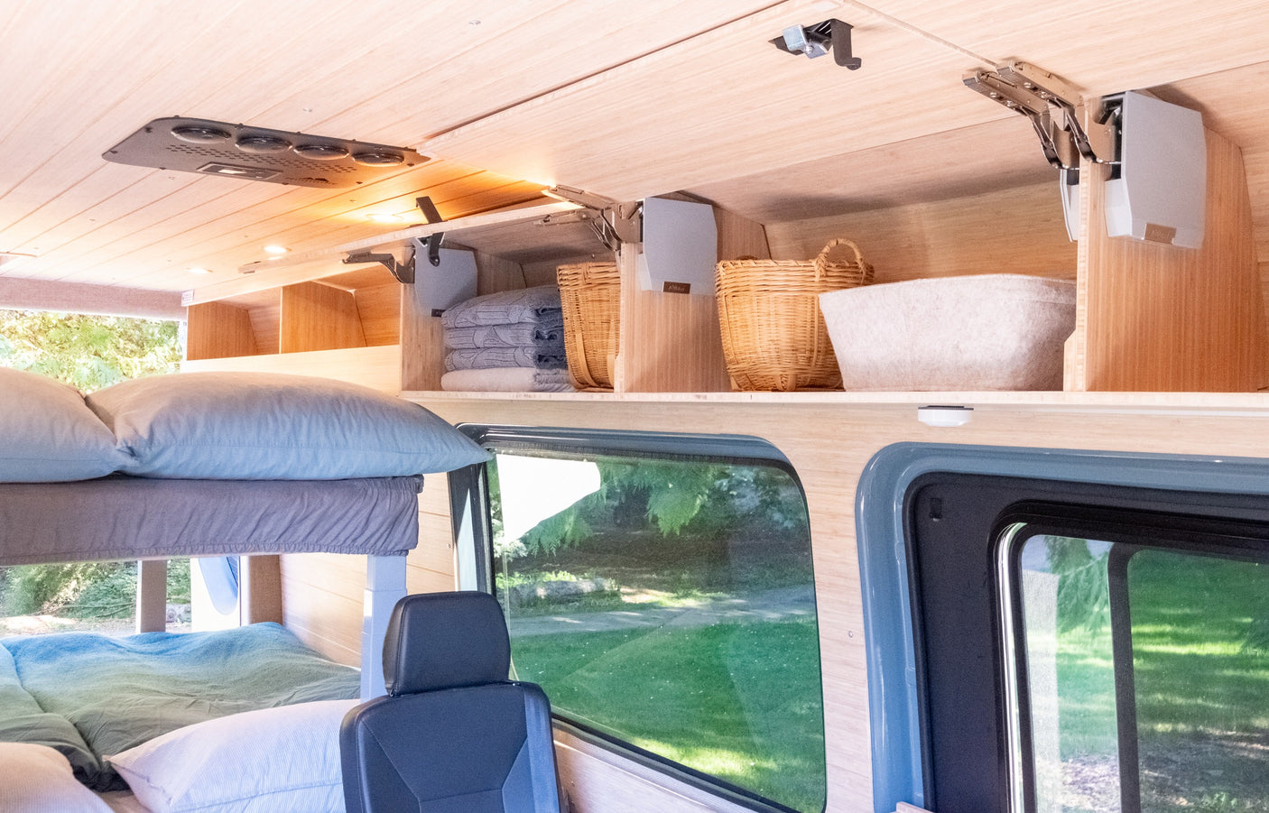 RV rental interior: bunk beds, wood paneling, and organized overhead storage with baskets. A scenic outdoor view.