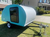 A compact teal & white teardrop camper, perfect for an rv rental, parked on a bright lawn by houses.