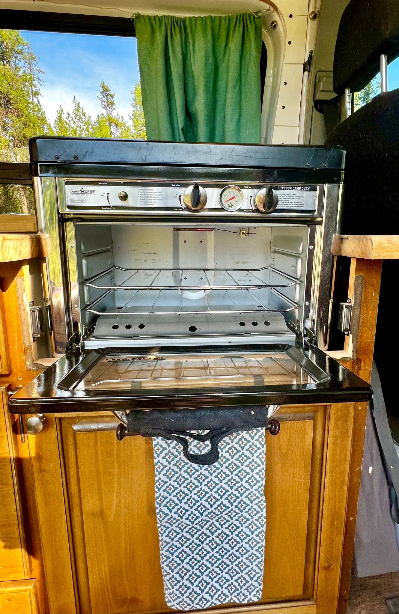 An RV rental's Camp Chef oven & stove, with an open door revealing racks, set in a cozy wooden kitchen. — photo 12