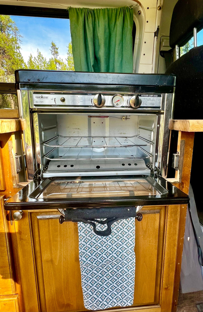An RV rental's Camp Chef oven & stove, with an open door revealing racks, set in a cozy wooden kitchen. — photo 12