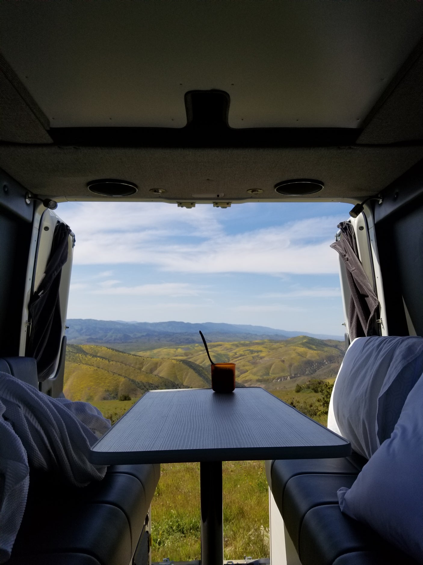 From an RV rental: cozy interior with a table & mug, framed by stunning rolling hills with yellow flowers.