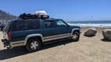 Green adventure SUV at the beach with kitesurfers. For road trips, an RV rental offers more space.