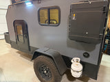 Explore with this rugged gray rv rental trailer, featuring a side door, window, mounted storage case, and propane tank.