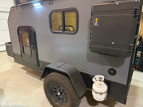 Explore with this rugged gray rv rental trailer, featuring a side door, window, mounted storage case, and propane tank.