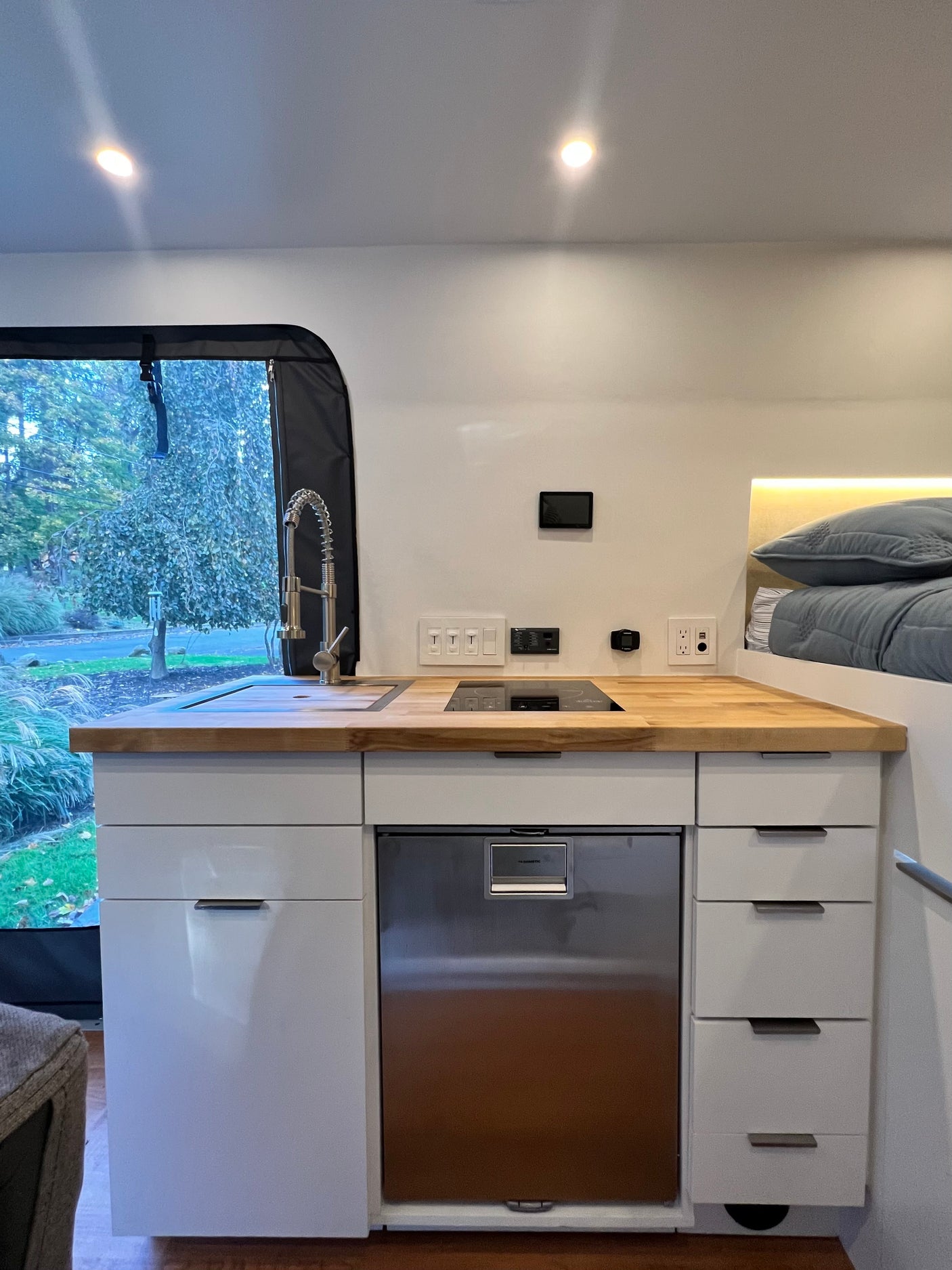 Modern rv rental interior: compact kitchen with sink, induction cooktop, fridge, and a cozy bed area.