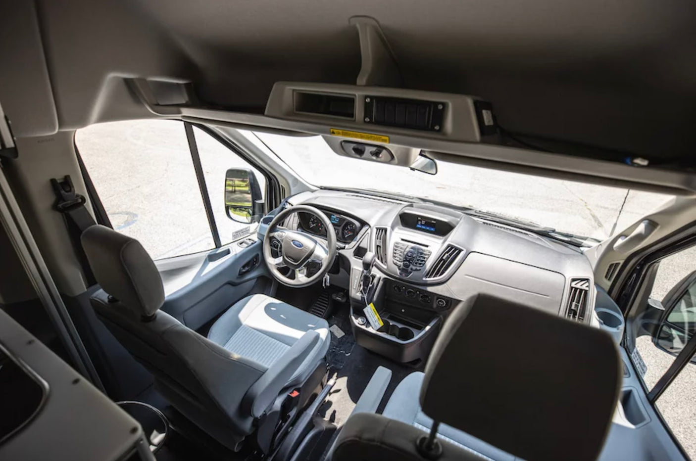 Inside an RV rental van: gray seats, steering wheel, and dashboard of the spacious driver's cabin are visible.