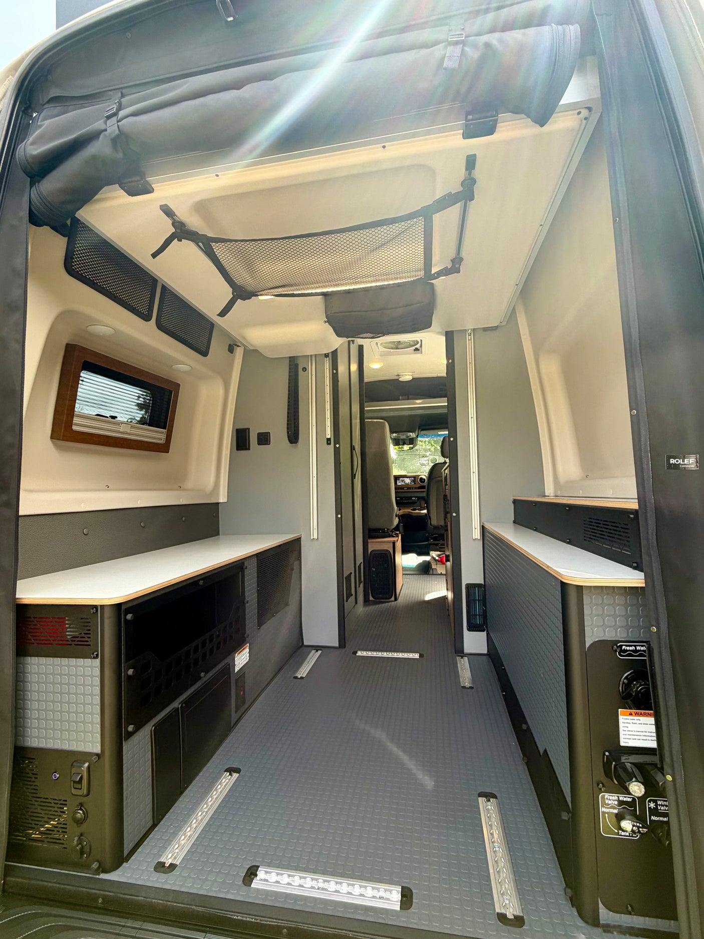 Clean & functional rv rental interior: custom cabinetry, durable flooring with tie-down tracks, window, and water system controls.