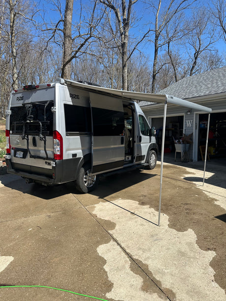 A silver RIZE camper van with an extended awning and bike rack, perfect for an rv rental outdoor adventure.