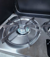Inside an RV rental: a stainless steel gas stove with one burner lit and a blue flame, ready for your adventures.