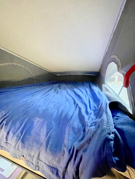 View of a cozy RV rental sleeping area: a blue patterned bed under the white pop-top ceiling.