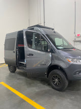 Gray Mercedes Sprinter camper van, featuring rugged tires and roof light bar, open side door. Ready for your next rv rental.