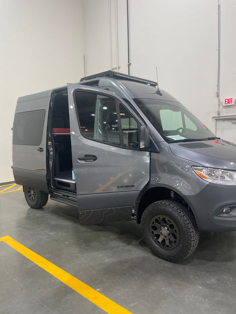 Gray Mercedes Sprinter camper van, featuring rugged tires and roof light bar, open side door. Ready for your next rv rental.