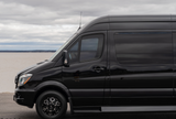 Sleek black luxury RV rental van parked by the water under a cloudy sky. Ready for your next road trip adventure.