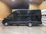 A glossy black rv rental van, likely a converted Ford Transit camper, parked in a warm, wood-paneled garage.